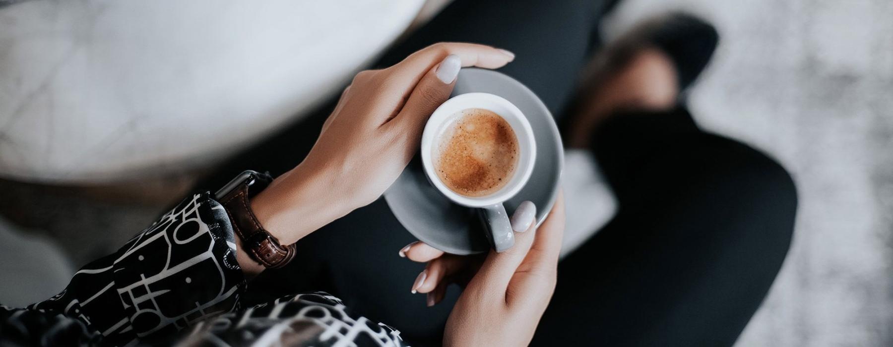 business woman sits next to a marble table with books and holds a saucer with a cup of espresso